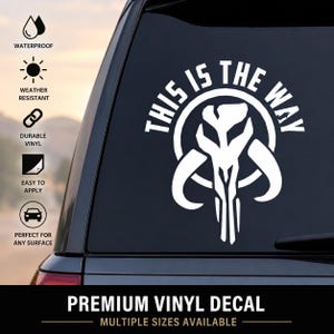May include: A white vinyl decal applied to a car window featuring a stylized Mandalorian mythosaur skull icon centered within a circular border, with the text THIS IS THE WAY arched in bold capital letters above the graphic design.
