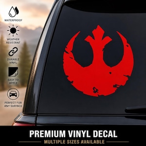 Può includere: Un adesivo in vinile rosso con il simbolo dell'Alleanza Ribelle e una texture usurata applicato sul finestrino di un'auto. L'immagine include icone per impermeabile, resistente alle intemperie, vinile durevole e il testo PREMIUM VINYL DECAL.