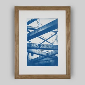 May include: A framed cyanotype photograph of a concrete structure with intersecting beams. The photograph is in a light wood frame.