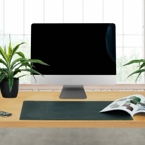 Könnte beinhalten: Eine dunkelgrüne Leder-Schreibtischunterlage auf einem Holztisch mit einem Computermonitor, einer Topfpflanze und einem Magazin auf der Unterlage.