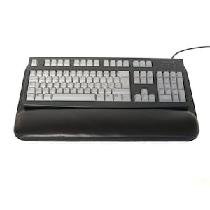 Puede incluir: Un teclado negro con un reposamuñecas. El teclado tiene una disposición estándar con teclas blancas y letras negras. El reposamuñecas está hecho de cuero negro.