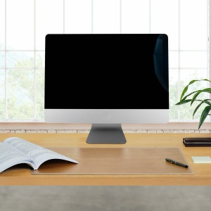 Könnte beinhalten: Eine braune Leder-Schreibtischunterlage mit einem genähten Rand, einem Stift und einem Magazin auf einem Holztisch mit einem Computermonitor im Hintergrund.