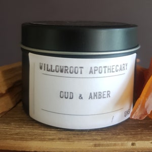 May include: A black tin candle with a white label that reads "Willowroot Apothecary Oud & Amber".