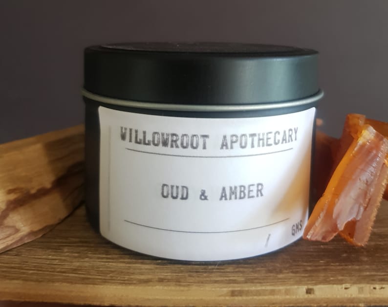 May include: A black tin candle with a white label that reads "Willowroot Apothecary Oud & Amber".