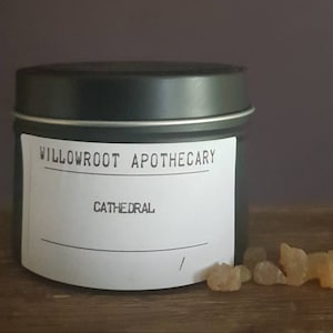 May include: A black metal tin candle with a white label that reads "Willowroot Apothecary" and "Cathedral".
