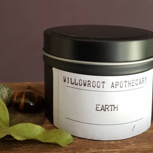 May include: A black metal tin candle with a white label that reads "Willowroot Apothecary" and "Earth".