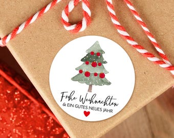 May include: A white round sticker with a watercolor illustration of a green Christmas tree with red ornaments. The text "Frohe Weihnachten & ein gutes neues Jahr" is written in black cursive script below the tree.