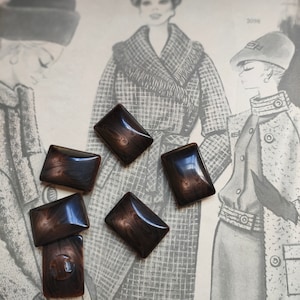 Puede incluir: Seis botones rectangulares marmoleados de color marrón y negro. Los botones están dispuestos en semicírculo sobre una superficie con estampado blanco y negro.