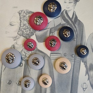 Op de afbeelding: Assortiment van 11 ronde knopen met een leeuwenkopontwerp. De knopen zijn in verschillende kleuren, waaronder rood, blauw, grijs en beige.