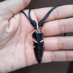 Op de afbeelding: Een zwarte obsidianen pijlpunt hanger aan een zwarte koordsnoer. De pijlpunt is gewikkeld met zilverdraad.