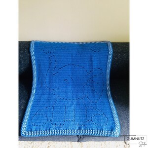 Puede incluir: Una manta de bebé de ganchillo azul con un borde blanco. La manta presenta un diseño simple de círculos.