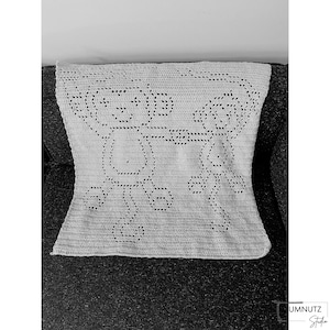 Könnte beinhalten: Eine weiße Häkeldecke mit geometrischem Muster. Die Decke liegt auf einem dunkelgrauen Sofa.