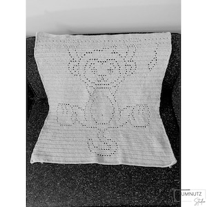 May include: A white crocheted baby blanket with a bear design. The blanket is made with a simple stitch and has a delicate, lacy look.