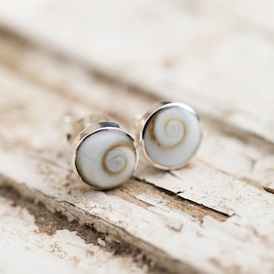 May include: A pair of silver stud earrings with a white shell inlay featuring a spiral pattern.