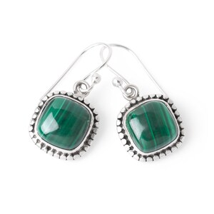May include: A pair of silver earrings with green malachite stones set in a square shape with a beaded border.