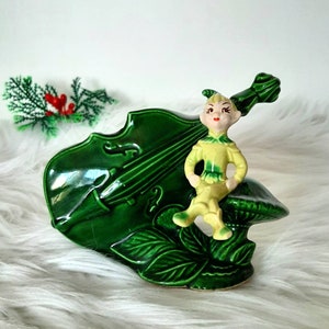 May include: A green ceramic figurine of a whimsical elf sitting on a mushroom with a green cello behind it.