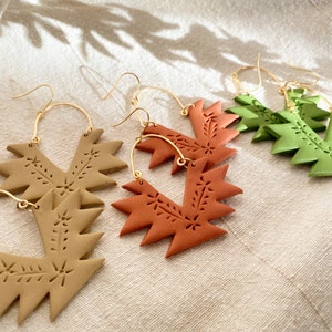 May include: Three pairs of geometric hoop earrings with a gold hook. The earrings are made of clay and have a floral design. The earrings are in shades of brown, orange, and green.