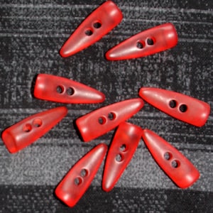 Könnte beinhalten: Zehn rote Plastikknöpfe mit jeweils zwei Löchern. Die Knöpfe sind spitz oval geformt und haben eine glänzende Oberfläche.