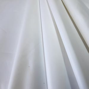 Op de afbeelding: Witte stof met een gladde textuur en een lichte glans. De stof is gevouwen op een manier die een reeks parallelle lijnen creëert.