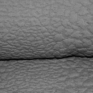 Könnte beinhalten: Nahaufnahme eines grauen, strukturierten Stoffes mit einem dezenten Muster. Der Stoff ist in der Mitte gefaltet und zeigt die Textur auf beiden Seiten.