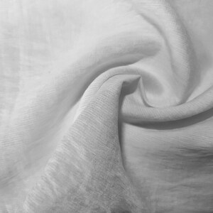 Peut inclure: Tissu blanc avec une texture lisse et soyeuse. Le tissu est plié et drapé, créant des plis et des rides doux.