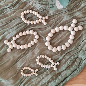 Könnte beinhalten: Fünf Holzperlen-Fisch-Ornamente in verschiedenen Größen, angeordnet auf einer grünen Stoffoberfläche. Der größte Fisch befindet sich in der Mitte, umgeben von den kleineren Fischen. Ein kleines Glasgefäß mit weißen Blumen und einem Etikett mit der Aufschrift "Taufe von Benji 16.06.2023" befindet sich im Hintergrund.