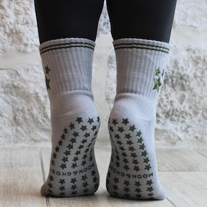 May include: Light grey socks featuring dark green star patterns on the soles and ankles. The cuffs have two dark green stripes and embroidered stars. The words "MOON & GHOST" are printed on the soles.