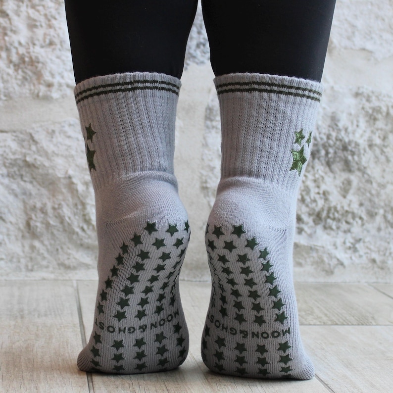 May include: Light grey socks featuring dark green star patterns on the soles and ankles. The cuffs have two dark green stripes and embroidered stars. The words "MOON & GHOST" are printed on the soles.