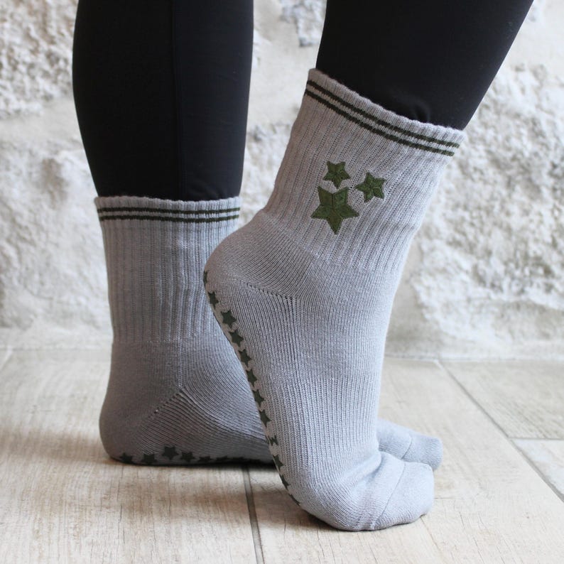 May include: Grey socks with green star designs and a green stripe at the top. The socks have a non-slip grip on the soles. The socks are ribbed and made of a soft material.