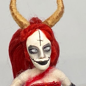Ona jest diabłem, z jaskrawoczerwonymi włosami i długą, wielokolorową, filcową sukienką w kolorze czerwonym, czarnym i różowym. Lalka-demon, lalka o wysokości 6 cali.