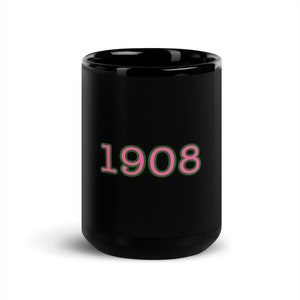 Puede incluir: Taza de café de cerámica negra con un contorno rosa y verde del número 1908.