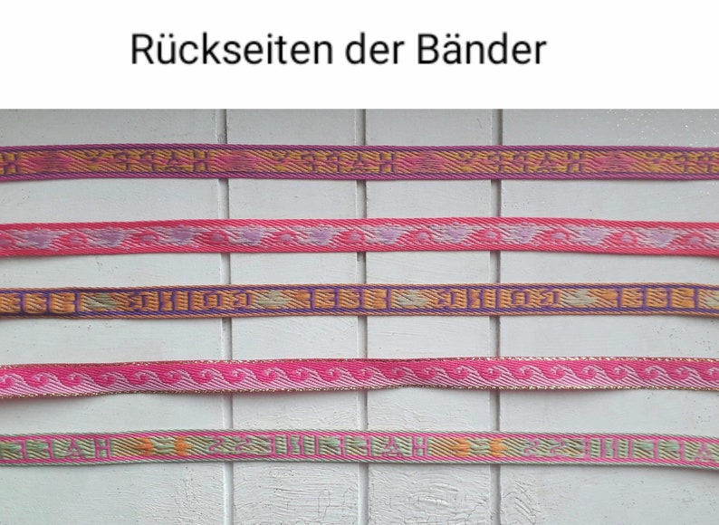 May include: Five different woven ribbon trims with various patterns and colours, including pink, purple, orange, and gold. The ribbons are displayed on a white wooden surface. The text "R&uuml;ckseiten der B&auml;nder" is visible at the top of the image.