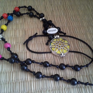 Könnte beinhalten: Eine schwarze Perlenkette mit bunten Perlen und einem silbernen Anhänger mit der Aufschrift "dream". Der Anhänger hat ein gelbes Blumenmuster und einen klaren Glaseinsatz.
