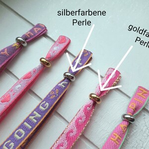 May include: Four colourful fabric wristbands with the words "Happy", "Going", and "Happy" printed on them. Each wristband has a silver or gold bead at the end.