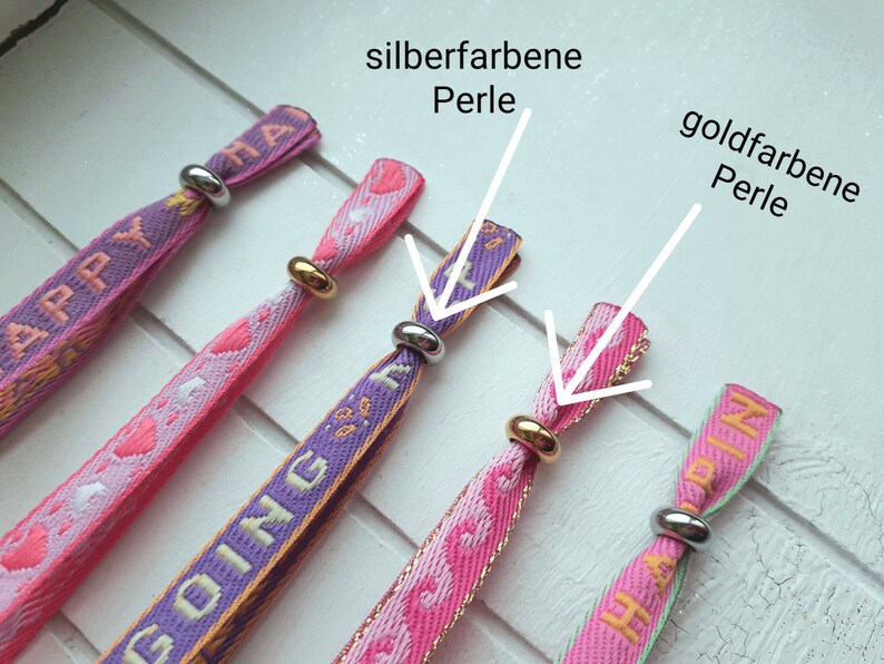 May include: Four colourful fabric wristbands with the words "Happy", "Going", and "Happy" printed on them. Each wristband has a silver or gold bead at the end.