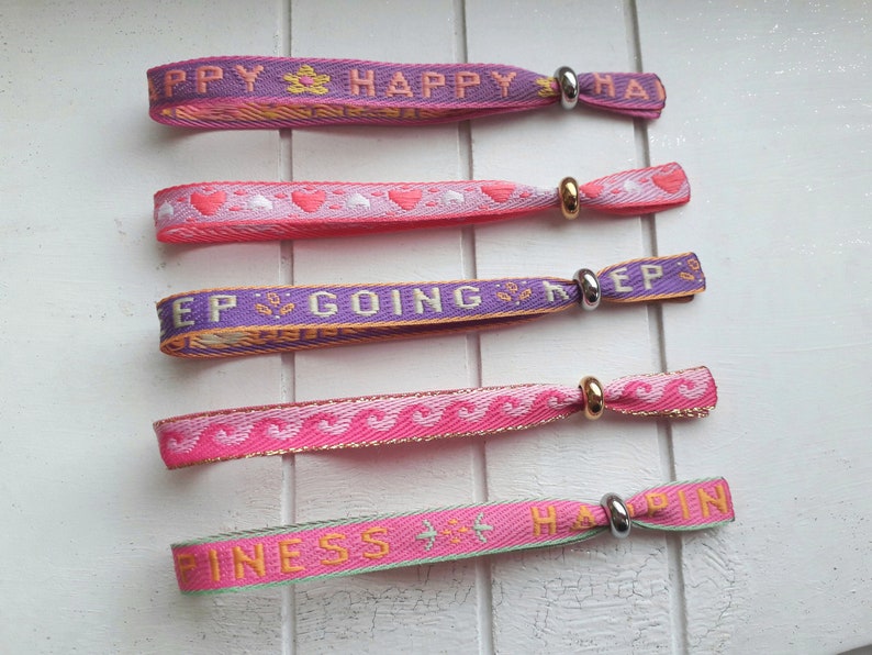 May include: Five colourful woven wristbands with different messages, including "Happy", "Keep Going", and "Happiness". Each band has a silver metal clasp.