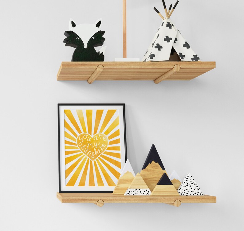 May include: A wooden shelf with a black and white fox figurine, a white teepee with black crosses, and a framed print with a yellow sunburst design and the text "You are my sunshine" in a white heart shape.