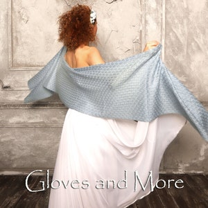 May include: A woman wearing a white dress and a light blue shawl with a textured pattern. The shawl is draped over her shoulders and flows behind her. The text "Gloves and More" is visible in the bottom center of the image.