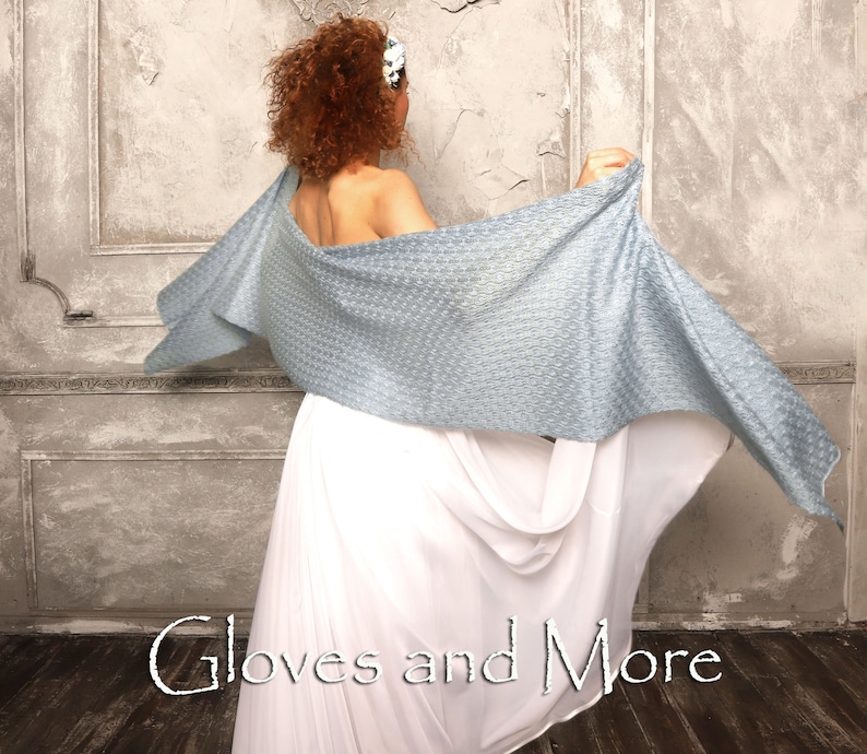 May include: A woman wearing a white dress and a light blue shawl with a textured pattern. The shawl is draped over her shoulders and flows behind her. The text "Gloves and More" is visible in the bottom center of the image.