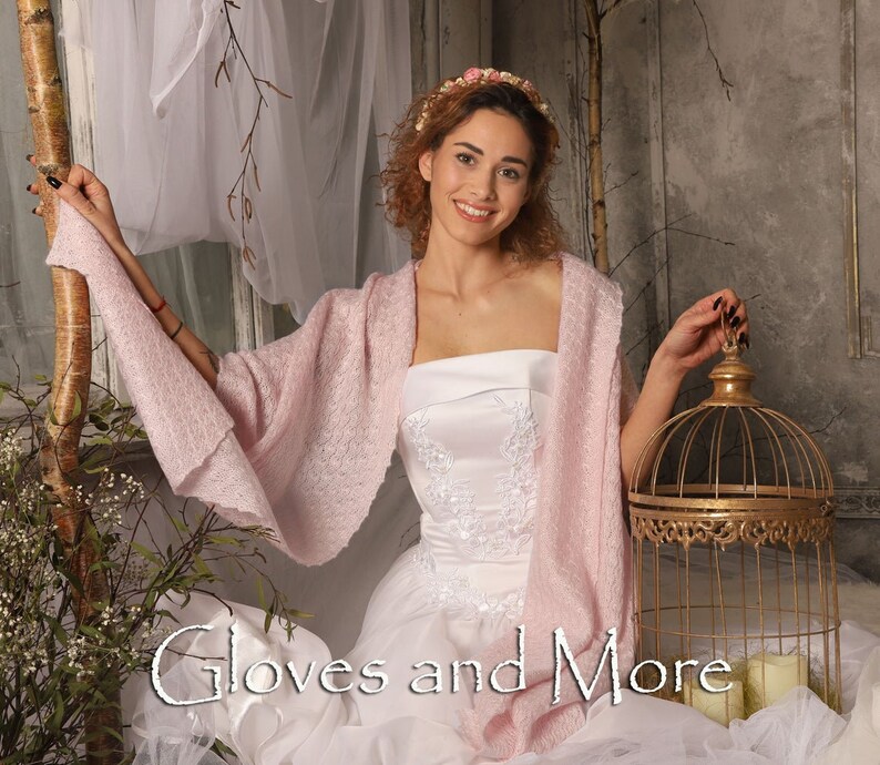 May include: A woman wearing a white strapless dress with a pink shawl and a flower crown. She is holding a gold birdcage. The text "Gloves and More" is visible in the image.