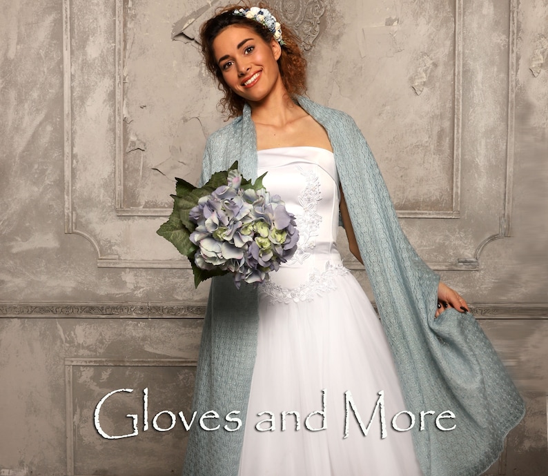 May include: A bride wearing a white strapless wedding dress with a light blue shawl and a flower crown. She is holding a bouquet of blue hydrangeas. The text "Gloves and More" is written in the bottom center of the image.