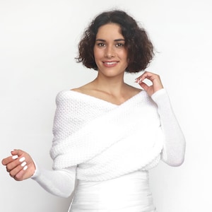 Puede incluir: Un su&eacute;ter blanco de hombros descubiertos con mangas largas y un dise&ntilde;o cruzado en la parte delantera.