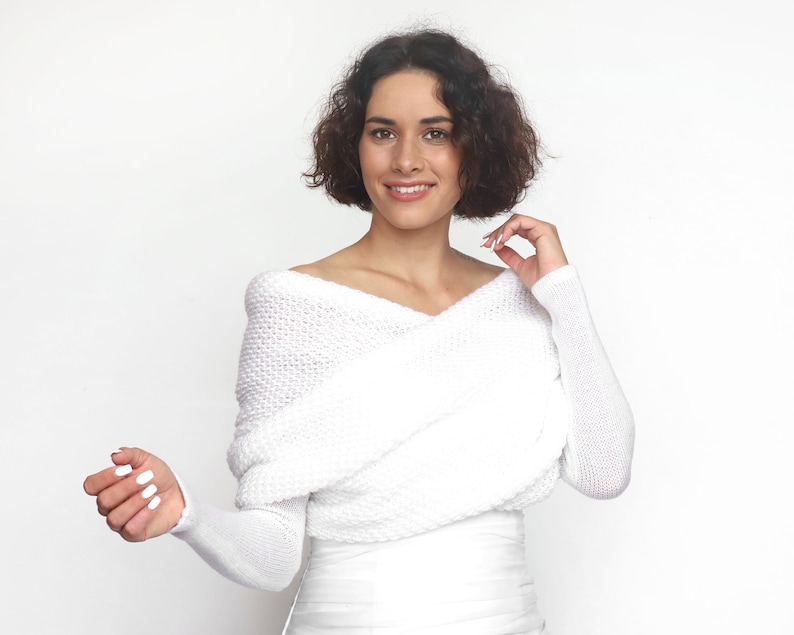 Puede incluir: Un su&eacute;ter blanco de hombros descubiertos con mangas largas y un dise&ntilde;o cruzado en la parte delantera.