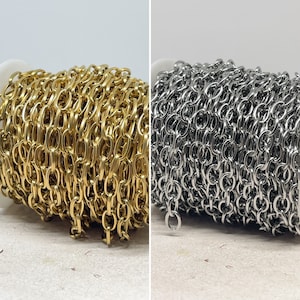Könnte beinhalten: Zwei Spulen Kette, eine gold und eine silber. Die Kette ist ein zartes, verlinktes Design.