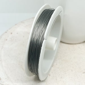 Könnte beinhalten: Eine Spule mit silberfarbenem Draht auf einer weißen Kunststoffspule. Der Draht ist fest um die Spule gewickelt.