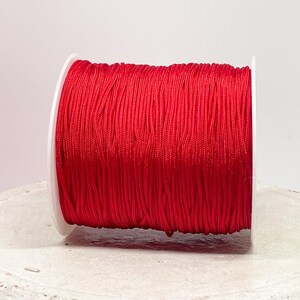 Könnte beinhalten: Eine Spule mit leuchtend rotem Garn, fest auf einer weißen Kunststoffspule gewickelt.