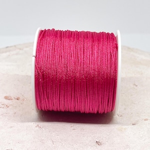 Könnte beinhalten: Eine Spule mit leuchtend pinkfarbenem gewachstem Garn, perfekt für die Schmuckherstellung oder Bastelarbeiten.