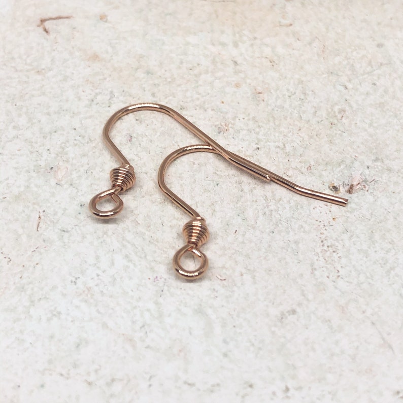 May include: Two rose gold earring hooks. The hooks are made of wire and have a small loop at the top. The hooks are designed to be used with earrings.