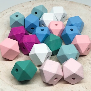 Op de afbeelding: Een verzameling geometrische houten kralen in verschillende pastelkleuren, waaronder roze, blauw, groen en wit. De kralen zijn allemaal even groot en hebben dezelfde vorm en een gladde, gepolijste afwerking.