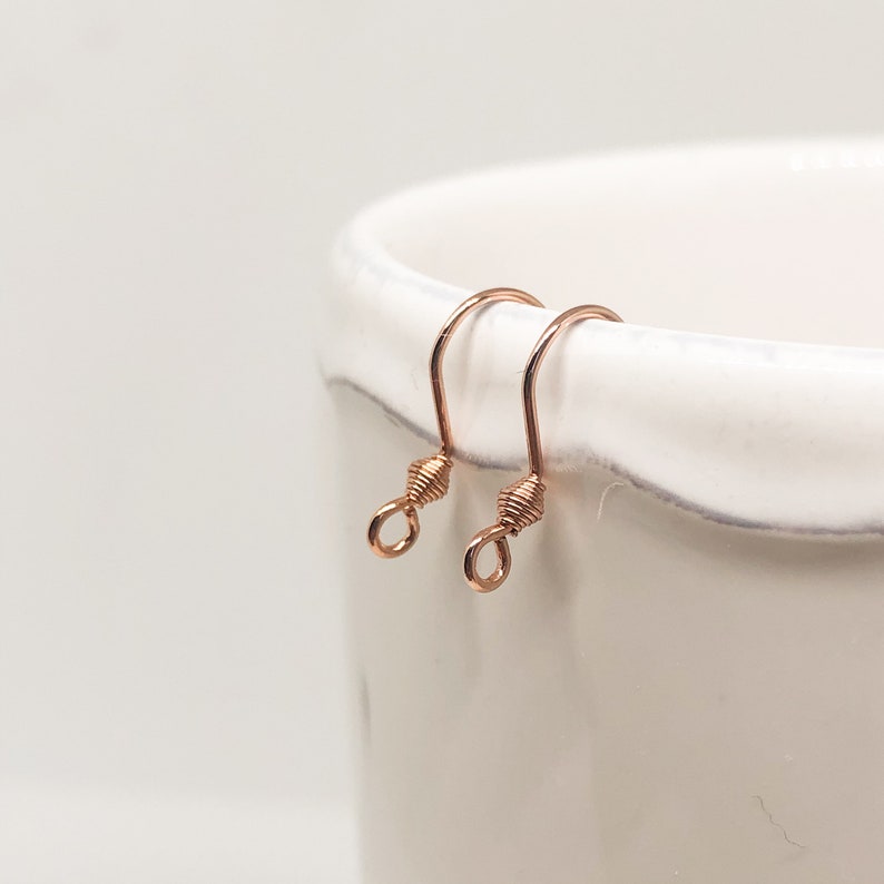 May include: Two rose gold earring hooks with a twisted wire design.
